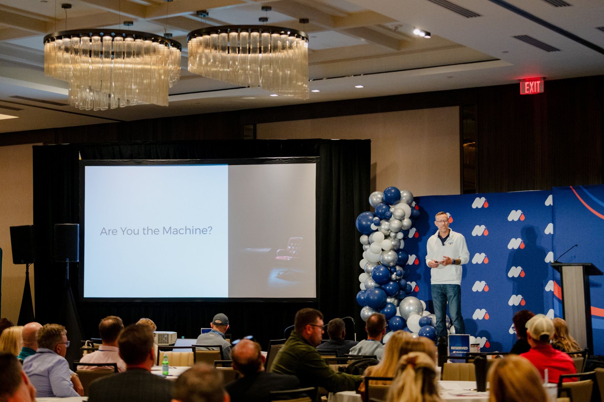 Travis on stage at MaxLawCon beside a slide reading: Are You the Machine?